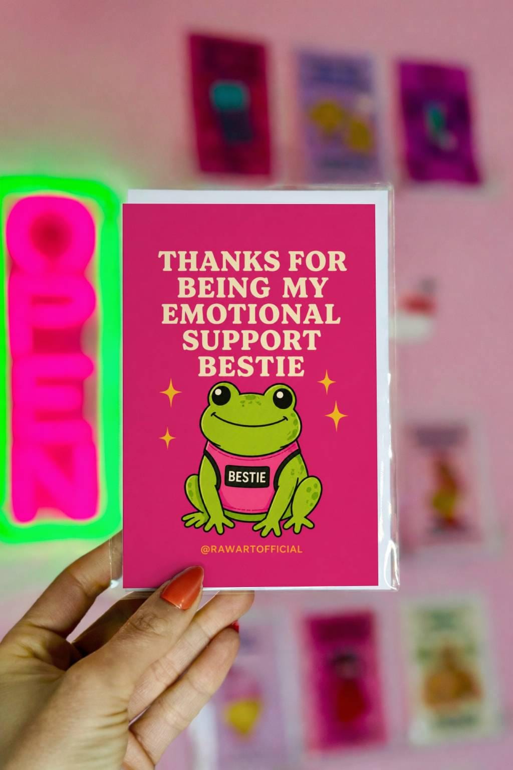 Funny friendship greeting card with smiling frog wearing “BESTIE” shirt on bright pink background saying “Thanks for being my emotional support bestie”