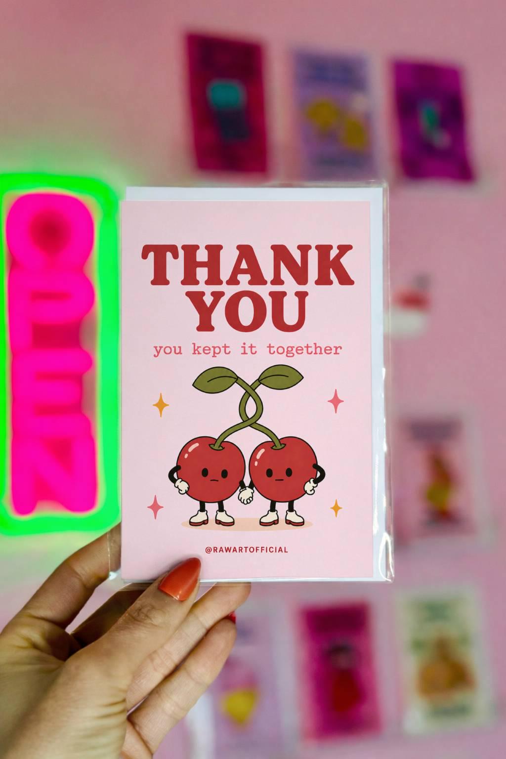Funny thank you greeting card with two cartoon cherries holding hands on pink background saying “Thank You, you kept it together”