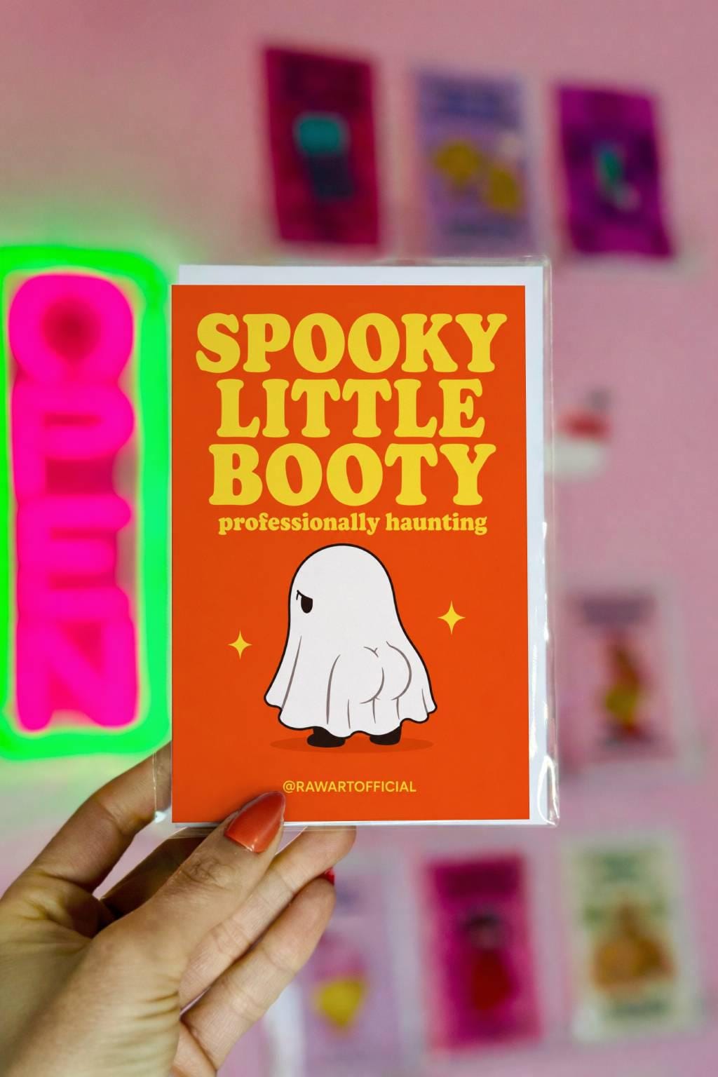 Funny Halloween greeting card with ghost showing a tiny booty on orange background saying “Spooky Little Booty professionally haunting”