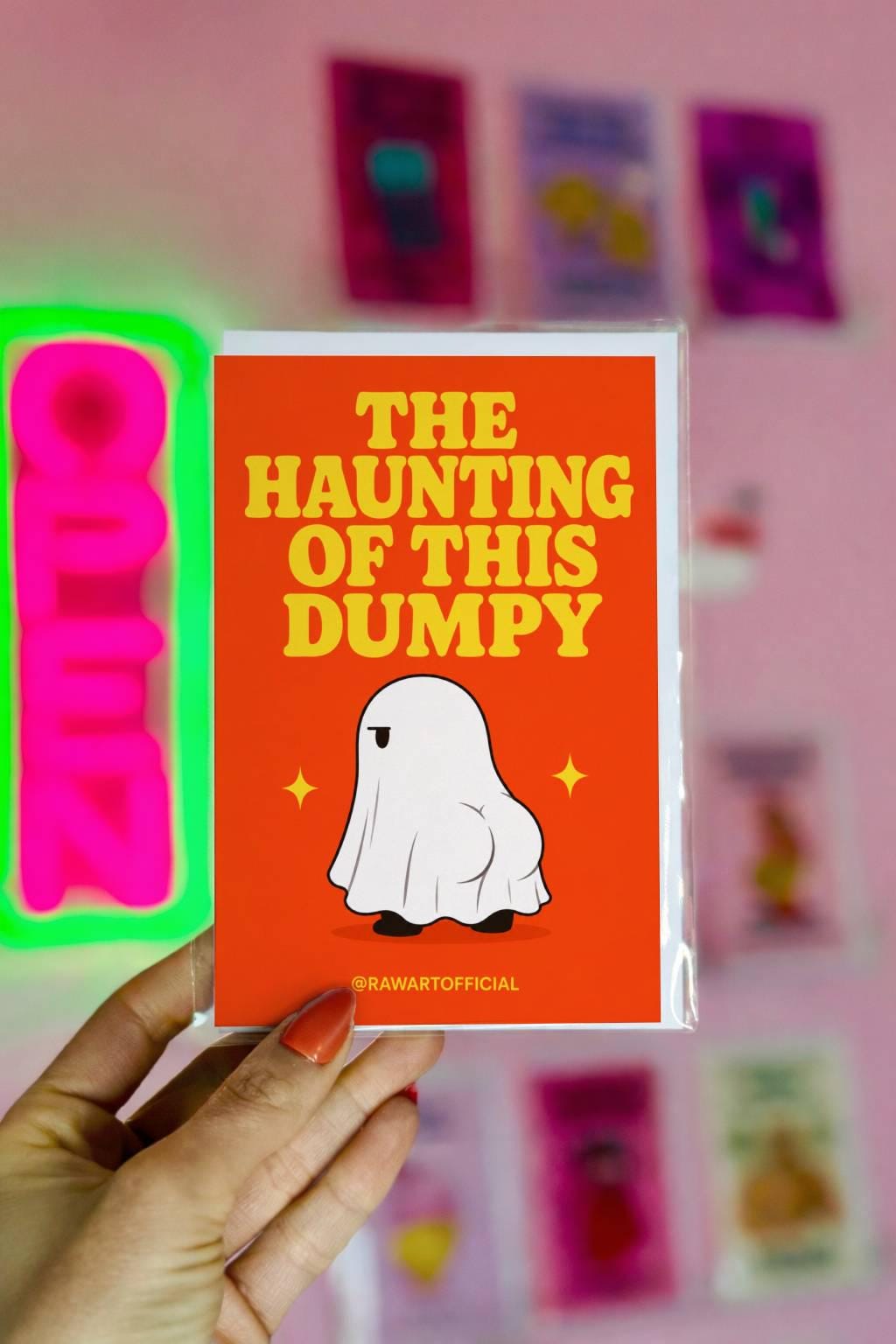 Funny Halloween greeting card with ghost showing a cheeky booty on orange background saying “The Haunting of This Dumpy”