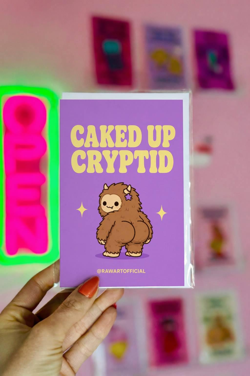 Funny Halloween greeting card with cute caked up cryptid Bigfoot character on lavender background saying “Caked Up Cryptid” in retro lettering.