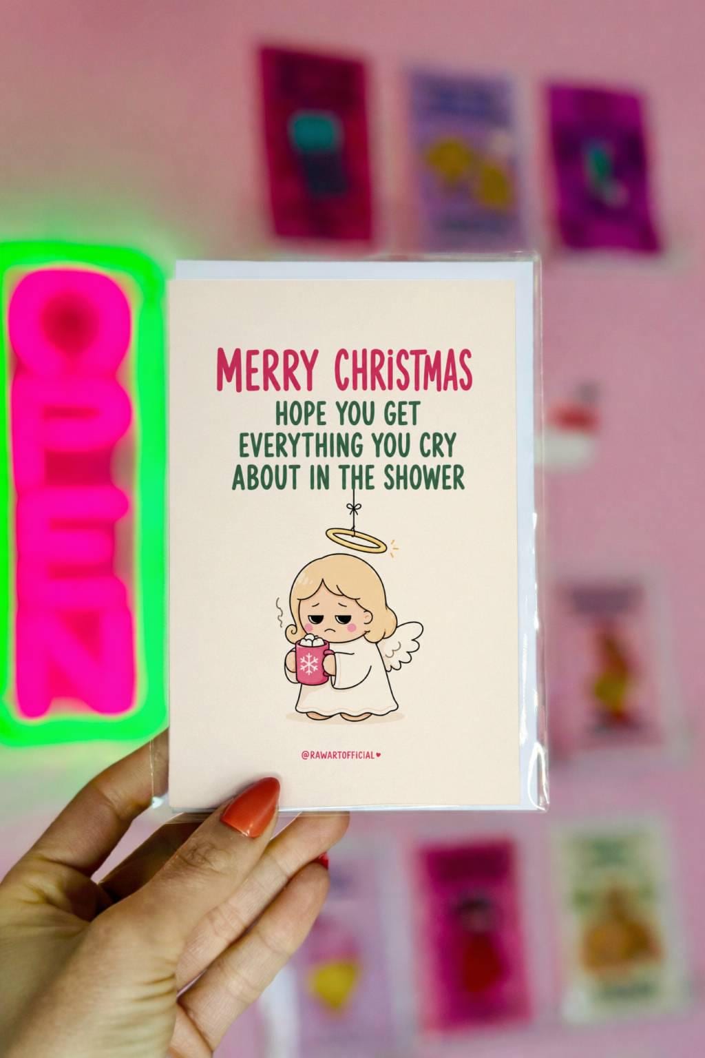 Funny Christmas card featuring a tired angel holding hot cocoa beside the phrase “Hope You Get Everything You Cry About In The Shower.”