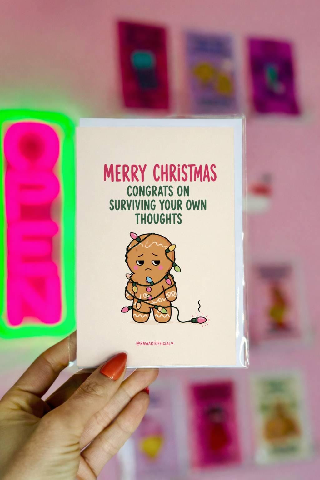 Funny Christmas card featuring a stressed gingerbread cookie tangled in Christmas lights beside the phrase “Congrats On Surviving Your Own Thoughts.”