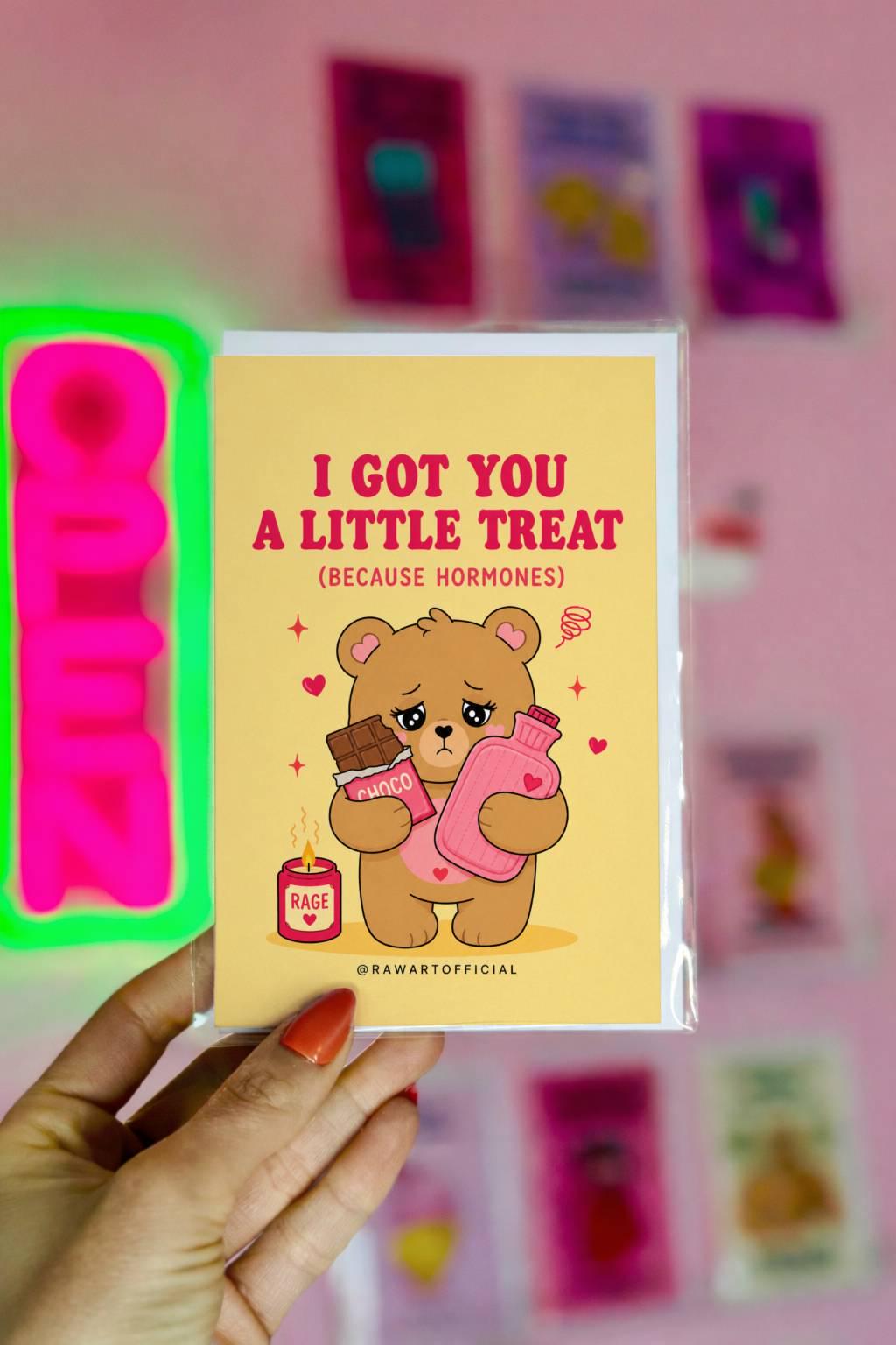 Funny PMS card featuring a stressed bear holding chocolate and a hot water bottle beside the phrase “I Got You A Little Treat (Because Hormones).”