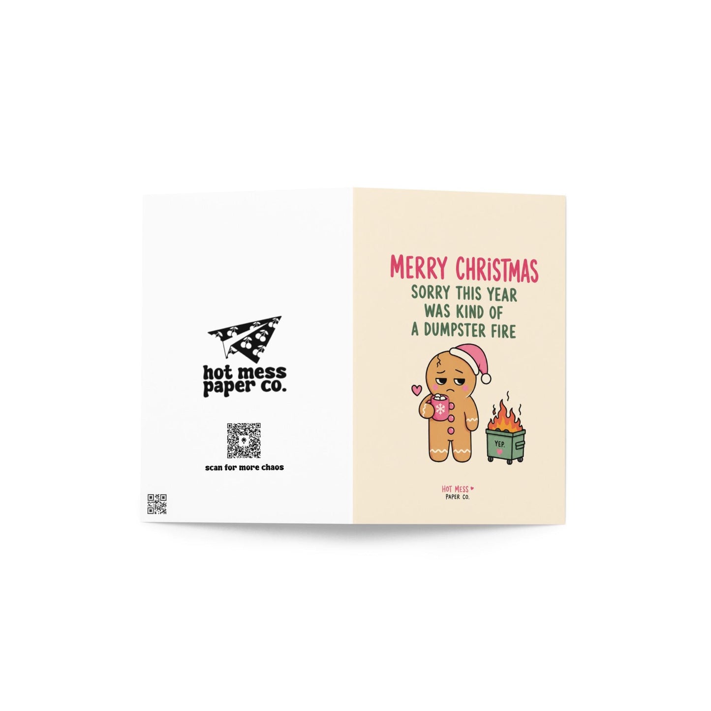 Funny Christmas card featuring a tired gingerbread cookie holding hot cocoa beside a tiny flaming dumpster with the phrase “Sorry This Year Was Kind Of A Dumpster Fire.”
