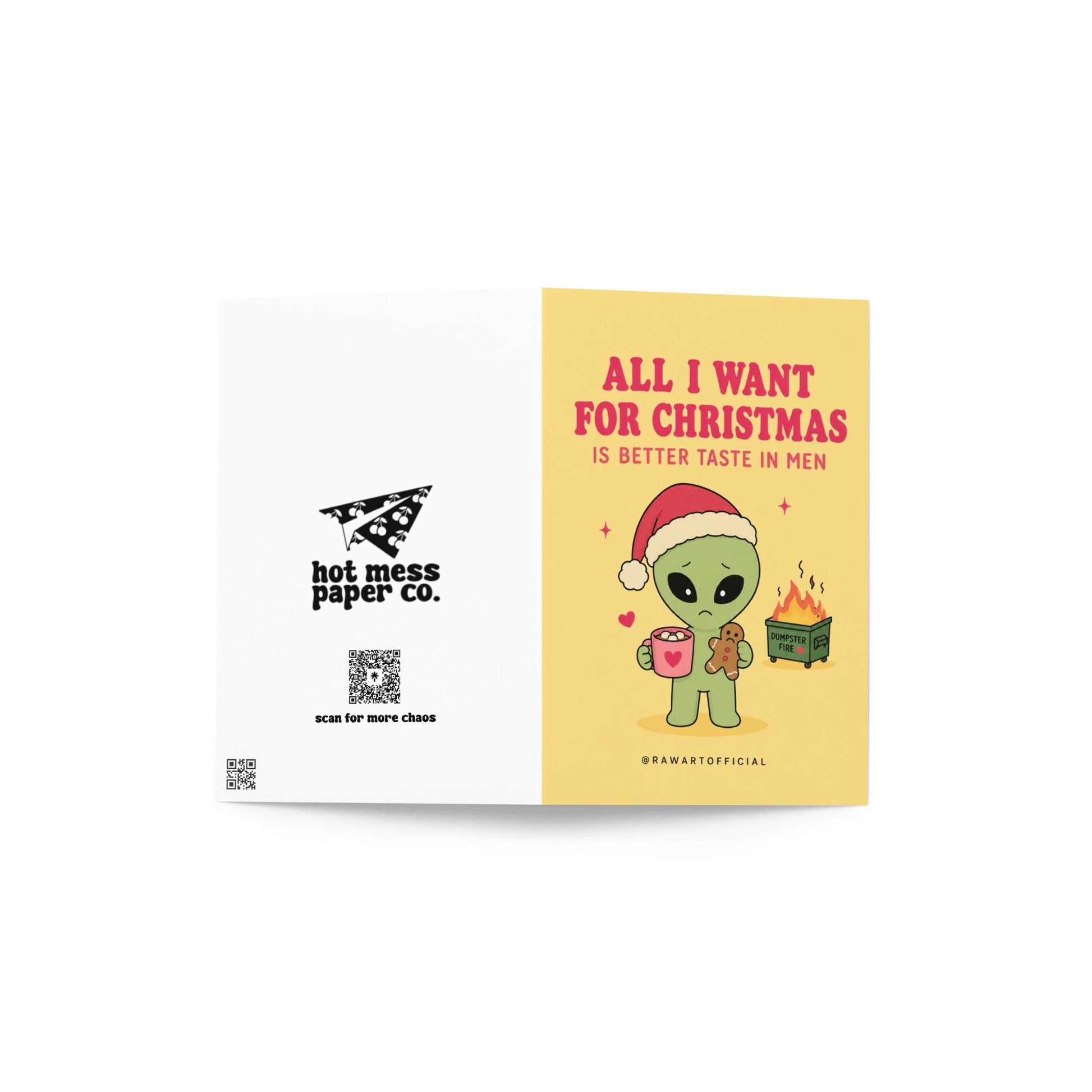 Funny Christmas card featuring a sad alien holding hot cocoa beside the phrase “All I Want For Christmas Is Better Taste In Men” with a tiny flaming dumpster.