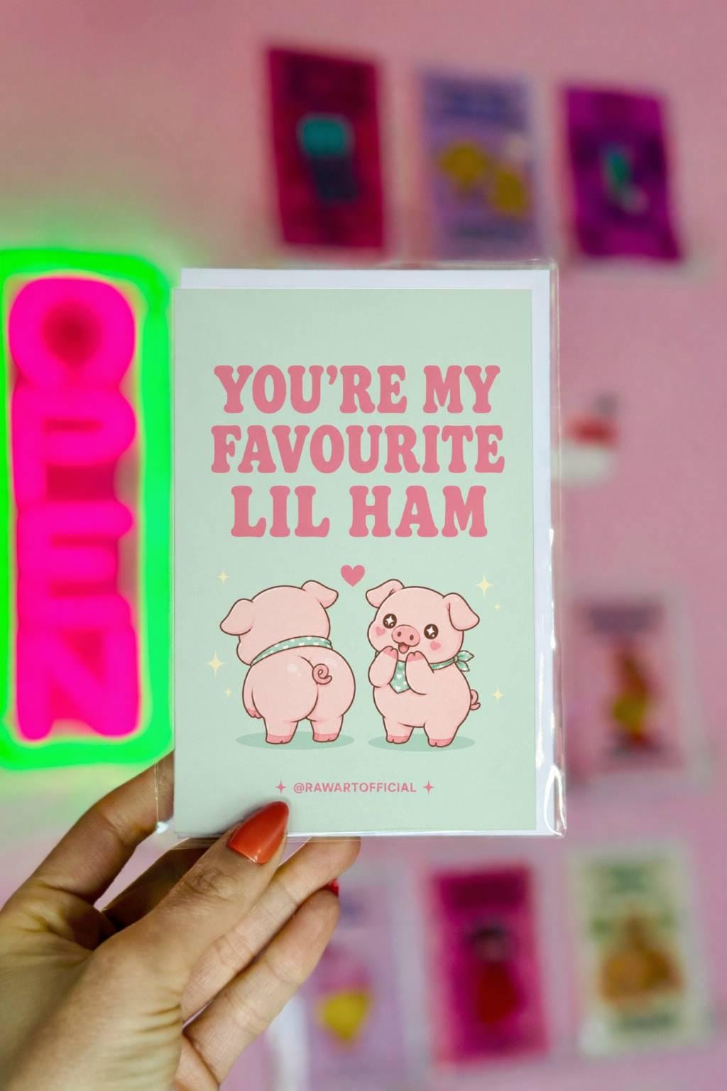Funny love card featuring two adorable pigs beside the phrase “You’re My Favourite Lil Ham,” including one cheeked-up pig and a heart above them.