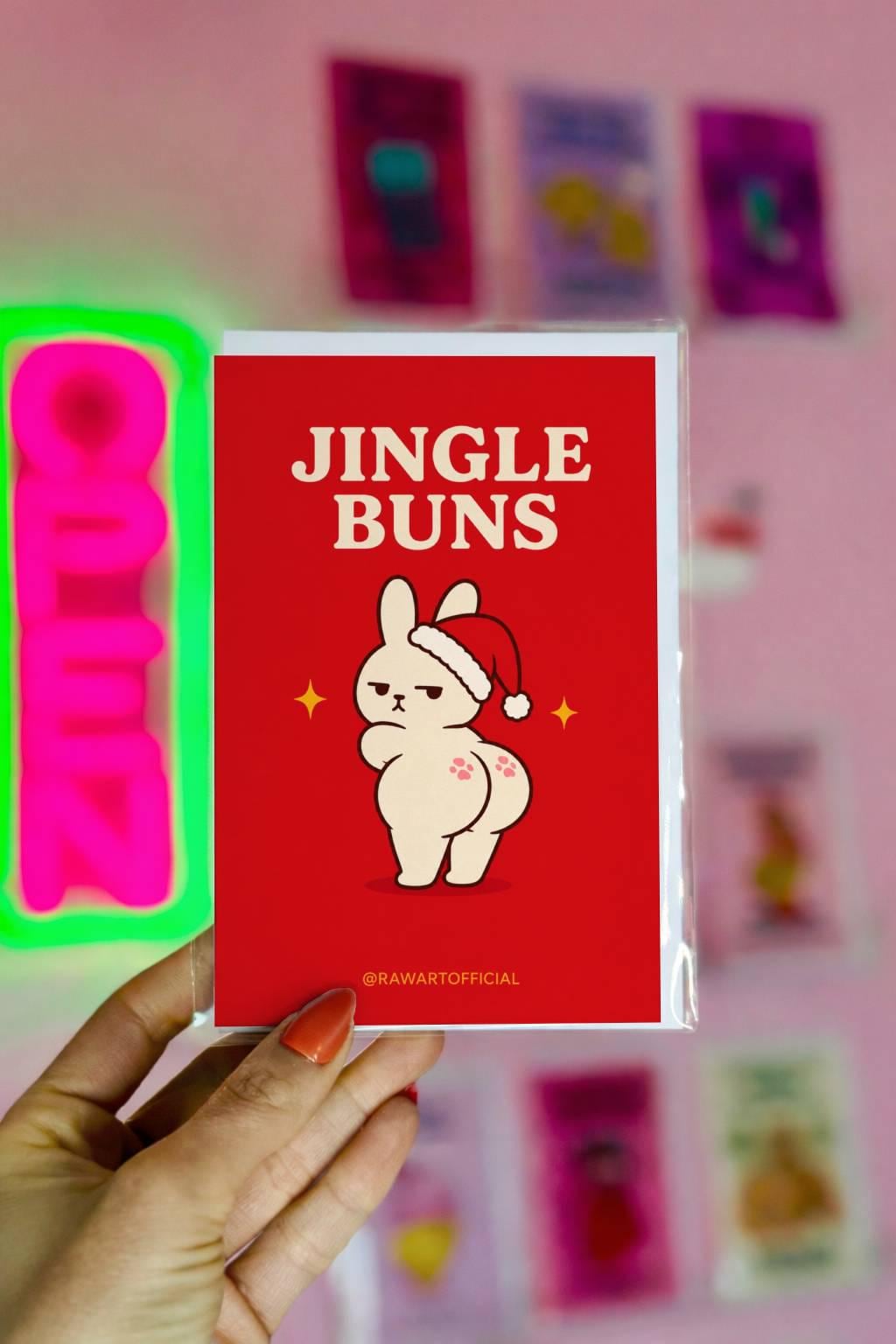 Funny Christmas card featuring a grumpy bunny in a Santa hat beside the phrase “Jingle Buns.”