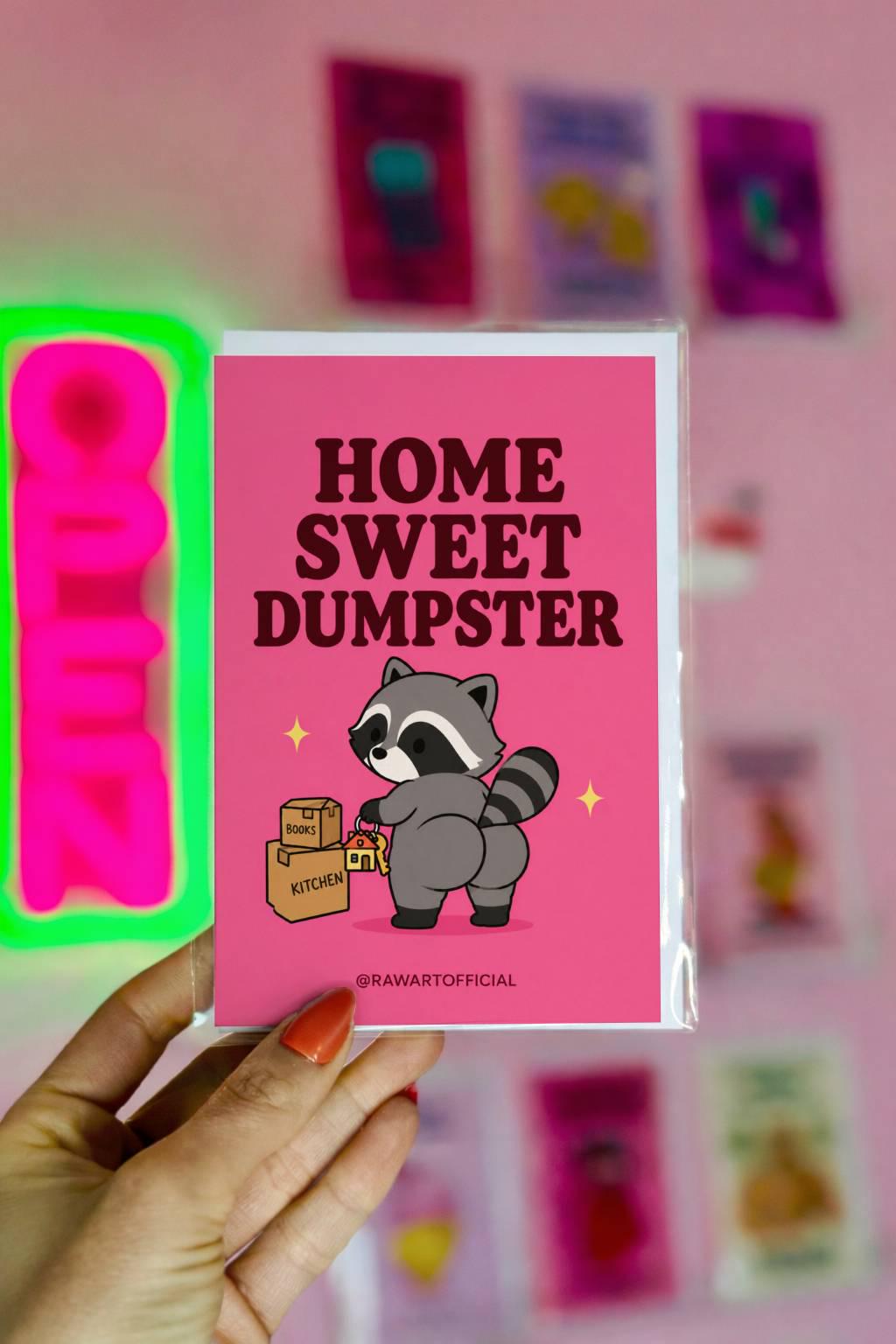 Funny new home card featuring a raccoon carrying house keys and moving boxes beside the phrase “Home Sweet Dumpster.” Humorous housewarming card.