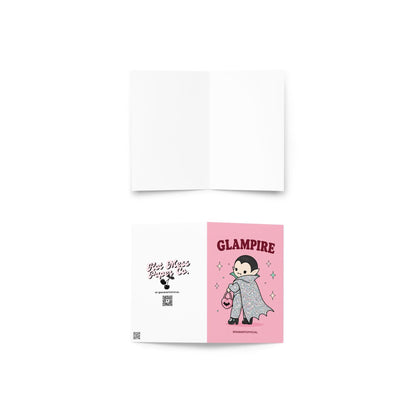 Pink Halloween greeting card reading "Glampire" featuring a cute glittery vampire wearing a glamorous cape and heels while carrying a pink heart-shaped bat purse surrounded by sparkles.