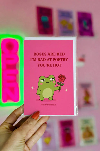 Funny Valentine card featuring a green frog holding a red rose beside the phrase “Roses Are Red, I’m Bad at Poetry, You’re Hot.”