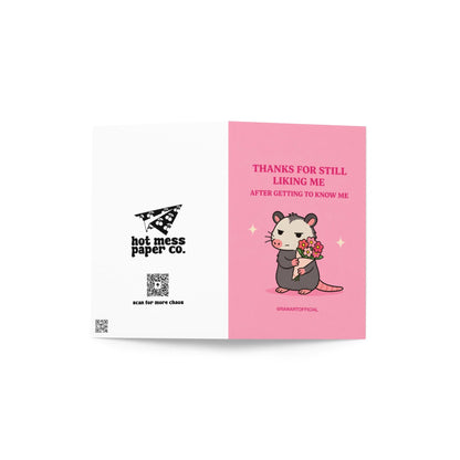 Funny greeting card featuring a grumpy opossum holding flowers beneath the phrase “Thanks for Still Liking Me After Getting to Know Me.”