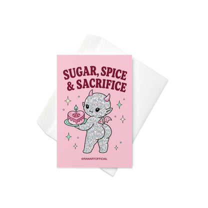 Pink funny Halloween greeting card reading “Sugar, Spice & Sacrifice” with a glittery cute devil holding a pink cake with a pentagram, photographed against a colorful pink card display.