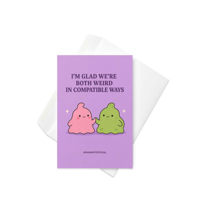 Funny love card featuring pink and green blob characters holding hands beneath the phrase “I’m Glad We’re Both Weird in Compatible Ways.”