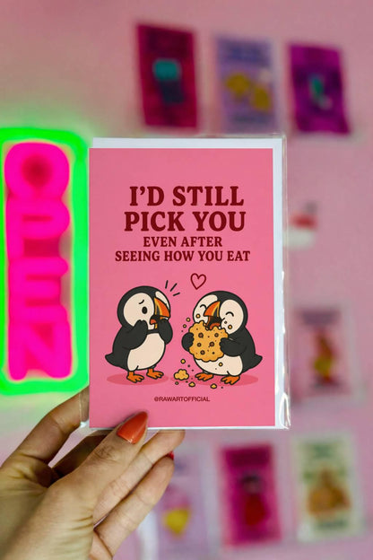Funny food lover card featuring two puffins, one messily eating a giant cookie, beside the phrase “I’d Still Pick You Even After Seeing How You Eat.”