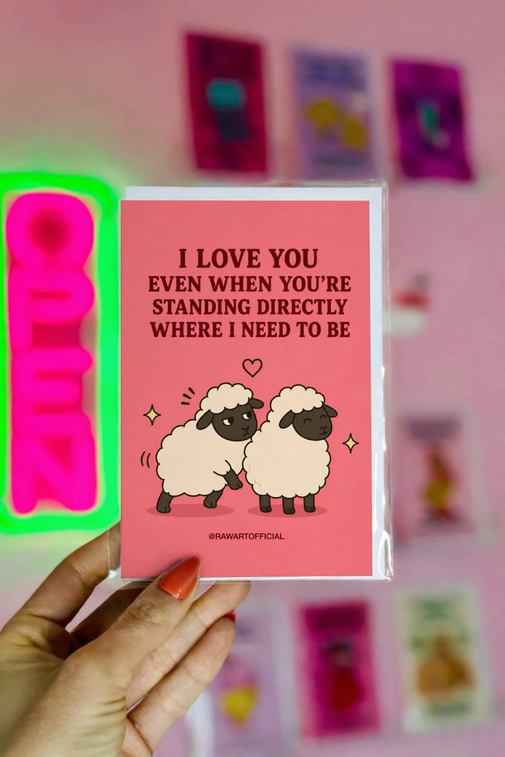 Funny couples card featuring two sheep standing close together beside the phrase “I Love You Even When You’re Standing Directly Where I Need to Be.”