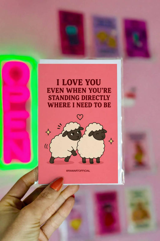 Funny couples card featuring two sheep standing close together beside the phrase “I Love You Even When You’re Standing Directly Where I Need to Be.”