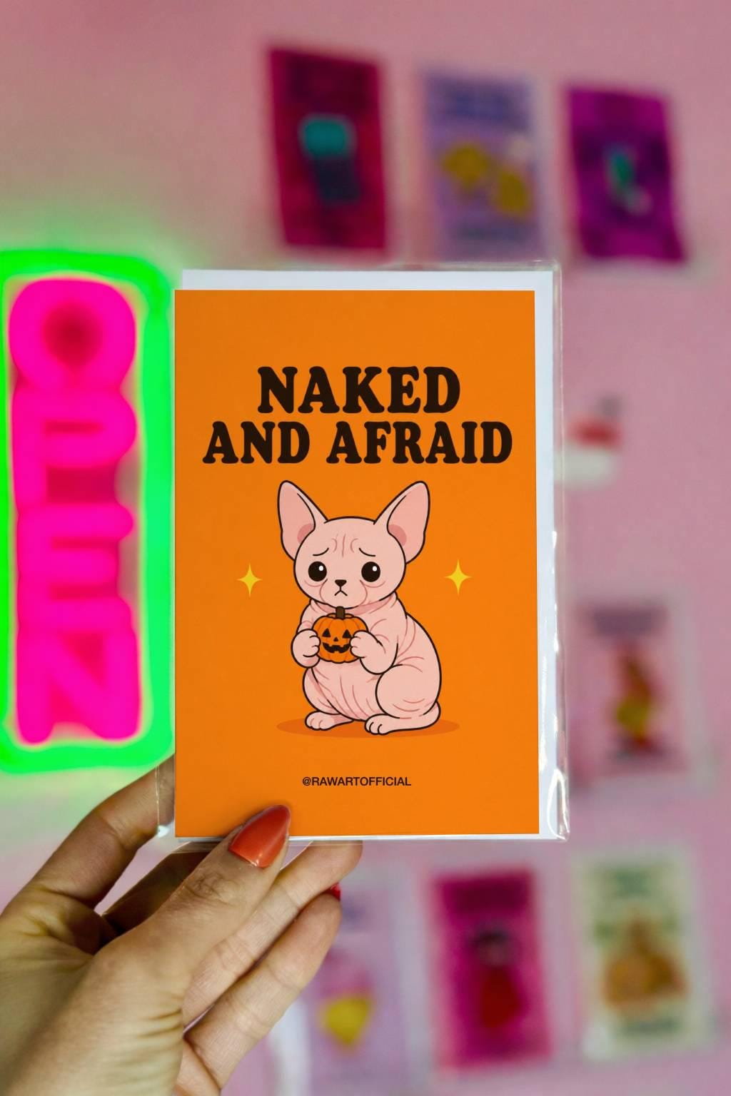 Funny Halloween greeting card featuring a worried pink hairless Sphynx cat holding a tiny jack-o’-lantern beneath the phrase “Naked and Afraid.” Perfect for hairless cat and Halloween lovers.