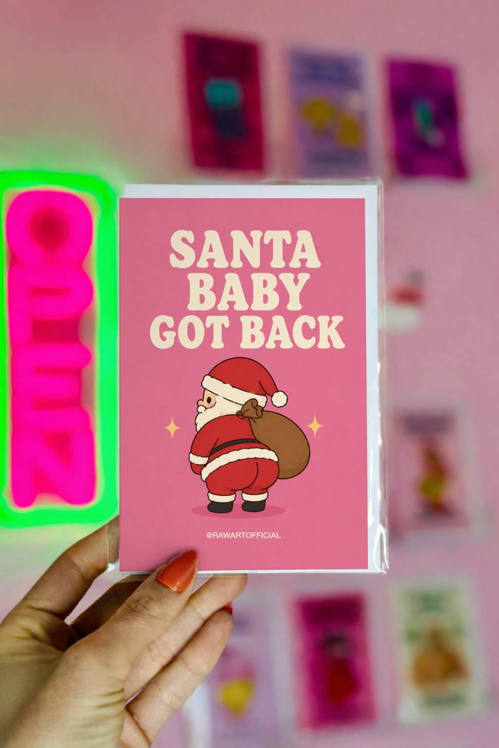 Funny Christmas card featuring Santa showing off his butt while carrying a sack of presents on a pink background with the phrase “Santa Baby Got Back.”