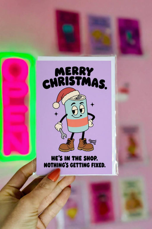Funny Christmas greeting card featuring a cartoon energy drink can wearing a red Santa hat, brown work boots, and white gloves while holding a wrench. Pastel lavender background with bold black retro lettering reading “Merry Christmas. He's in the Shop. Nothing's Getting Fixed.” Humorous holiday card for mechanics, oilfield workers, tradesmen, and garage enthusiasts.