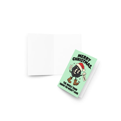 Funny Christmas greeting card featuring a smiling black lump of coal wearing a red Santa hat and brown cowboy boots, flashing a peace sign and holding a naughty list tag. Mint-green background with bold black retro lettering reading “Merry Christmas. The Whole Town Knows You Weren't Good.” Humorous small-town holiday card inspired by Christmas gossip and Santa's naughty list.