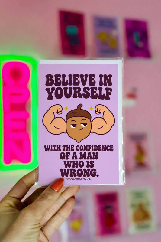 Funny encouragement greeting card with a pastel lavender background and bold dark purple retro lettering reading “Believe in Yourself With the Confidence of a Man Who Is Wrong.” Features a smug cartoon acorn flexing oversized muscular arms with golden sparkles. Sarcastic motivational humor by Hot Mess Paper Co.