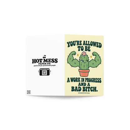 Funny encouragement greeting card featuring a green cartoon cactus flexing oversized muscular arms, with a smug expression, tiny pink flower, and terracotta pot. Pale yellow background with bold dark green retro lettering reading “You're Allowed to Be a Work in Progress and a Bad Bitch.” Humorous self-love and confidence card by Hot Mess Paper Co.