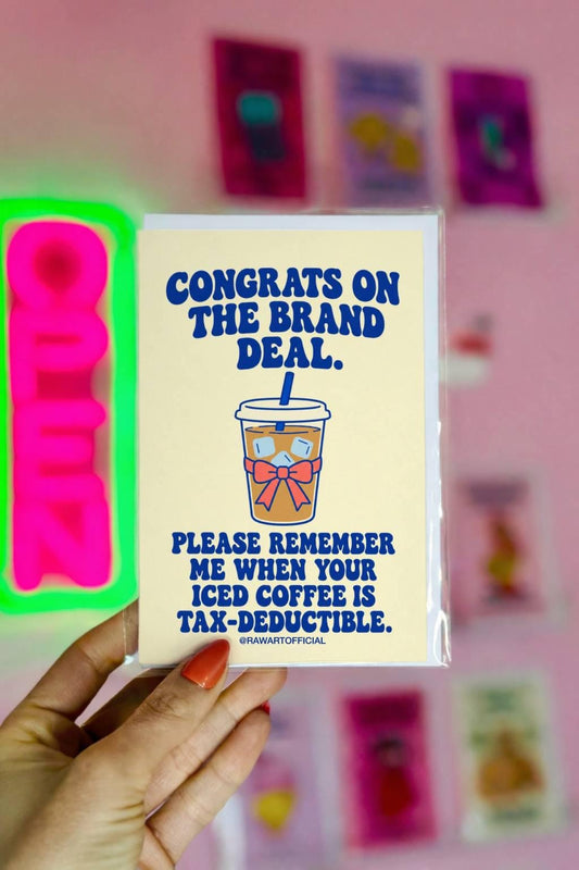 Funny influencer congratulations greeting card featuring a takeaway iced coffee cup with a blue straw, ice cubes, and pink bow on a pale yellow background. Bold blue retro lettering reads “Congrats on the Brand Deal. Please Remember Me When Your Iced Coffee Is Tax-Deductible.” Humorous celebration card for influencers, content creators, and social media brand collaborations by Hot Mess Paper Co.
 Copy alt text