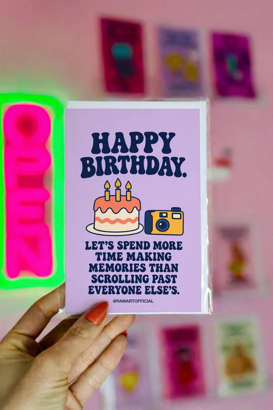 Thoughtful birthday greeting card featuring a frosted birthday cake with three lit candles beside a yellow and navy retro camera on a pastel lavender background. Bold navy lettering reads “Happy Birthday. Let's Spend More Time Making Memories Than Scrolling Past Everyone Else's.” Birthday card celebrating less screen time, friendship, and making real-life memories by Hot Mess Paper Co.