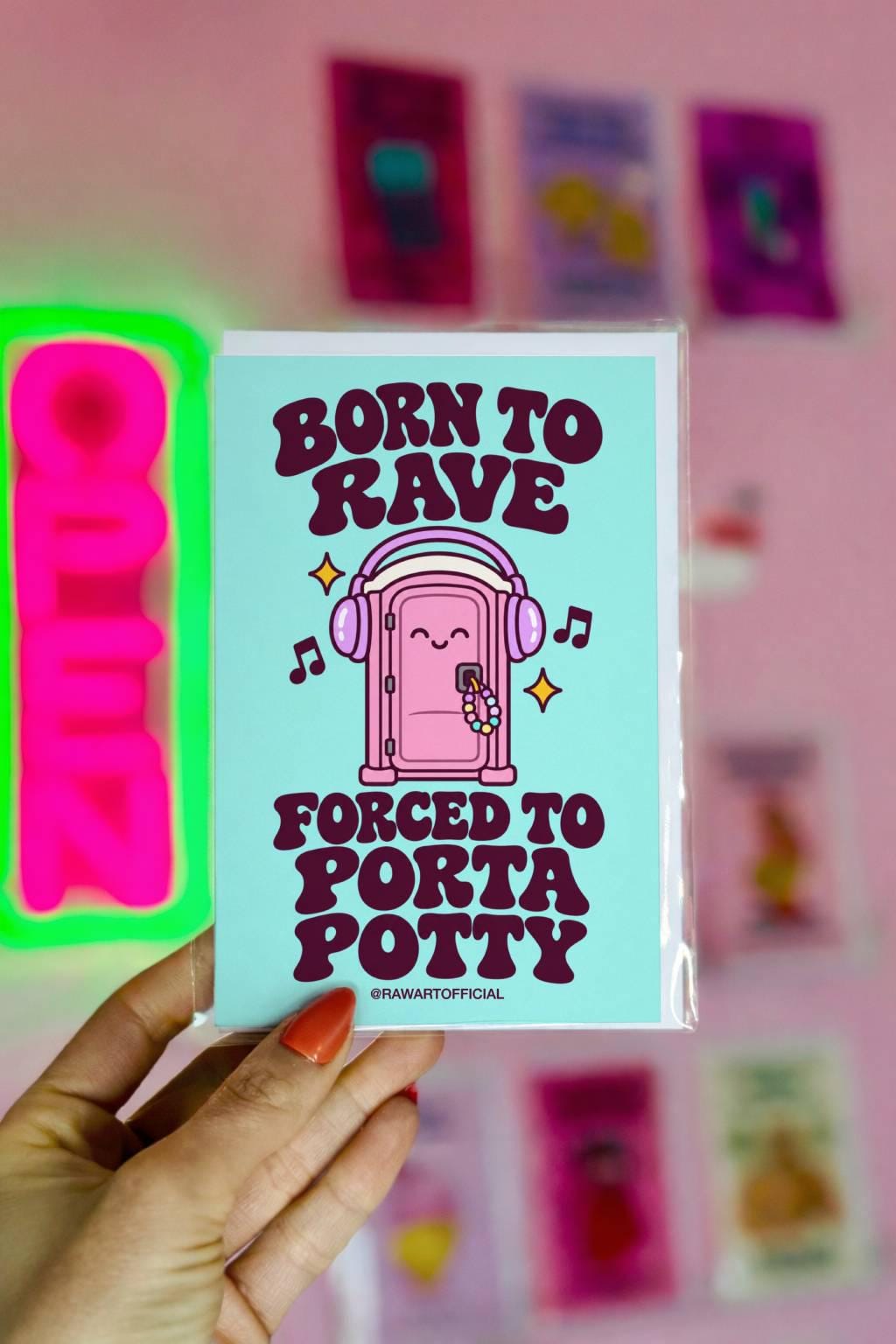 Funny rave festival card featuring a smiling pink porta potty wearing oversized purple headphones with colourful kandi bracelets hanging from its door. Musical notes and yellow sparkles surround the illustration against a bright mint-green background. Bold retro purple lettering reads “Born to Rave, Forced to Porta Potty.” Humorous EDM greeting card for music festival lovers and rave besties.