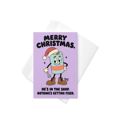 Funny Christmas greeting card featuring a cartoon energy drink can wearing a red Santa hat, brown work boots, and white gloves while holding a wrench. Pastel lavender background with bold black retro lettering reading “Merry Christmas. He's in the Shop. Nothing's Getting Fixed.” Humorous holiday card for mechanics, oilfield workers, tradesmen, and garage enthusiasts.