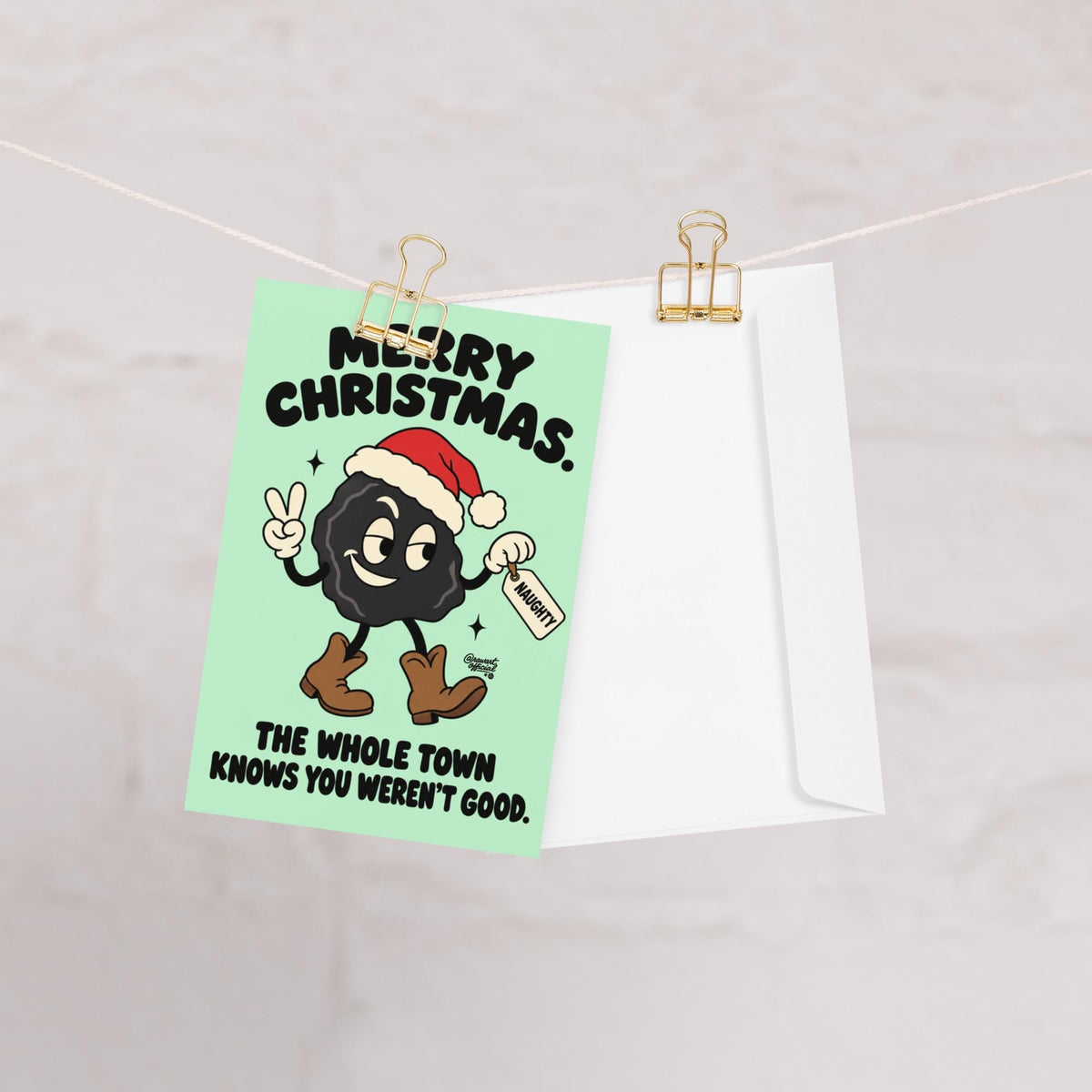 Funny Christmas greeting card featuring a smiling black lump of coal wearing a red Santa hat and brown cowboy boots, flashing a peace sign and holding a naughty list tag. Mint-green background with bold black retro lettering reading “Merry Christmas. The Whole Town Knows You Weren't Good.” Humorous small-town holiday card inspired by Christmas gossip and Santa's naughty list.