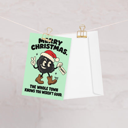 Funny Christmas greeting card featuring a smiling black lump of coal wearing a red Santa hat and brown cowboy boots, flashing a peace sign and holding a naughty list tag. Mint-green background with bold black retro lettering reading “Merry Christmas. The Whole Town Knows You Weren't Good.” Humorous small-town holiday card inspired by Christmas gossip and Santa's naughty list.