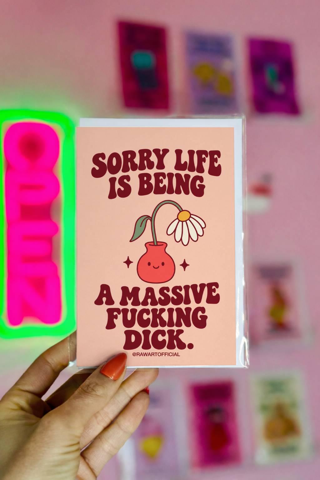Unconventional sympathy greeting card with a peach background and bold burgundy retro lettering reading “Sorry Life Is Being a Massive Fucking Dick.” Features a drooping white daisy with a yellow centre in a smiling coral-pink vase, surrounded by small decorative sparkles. A sweary sympathy card for comforting a friend through grief, heartbreak, or difficult times.