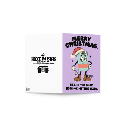 Funny Christmas greeting card featuring a cartoon energy drink can wearing a red Santa hat, brown work boots, and white gloves while holding a wrench. Pastel lavender background with bold black retro lettering reading “Merry Christmas. He's in the Shop. Nothing's Getting Fixed.” Humorous holiday card for mechanics, oilfield workers, tradesmen, and garage enthusiasts.