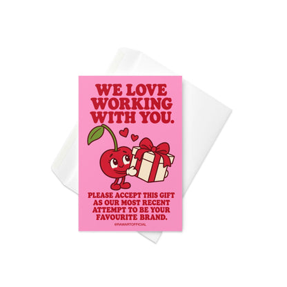 Pink influencer appreciation greeting card with bold red retro lettering reading “We Love Working With You. Please Accept This Gift as Our Most Recent Attempt to Be Your Favourite Brand.” Features a cute smiling red cartoon cherry holding a white gift box tied with a red ribbon, with two floating hearts. A playful brand collaboration thank you card for content creators and influencer PR packages.