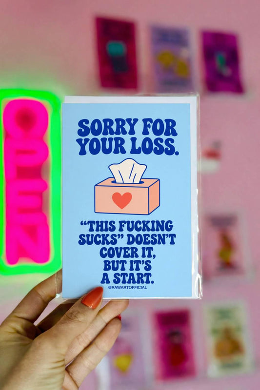Unconventional sympathy greeting card with a pastel blue background and bold dark blue retro lettering reading “Sorry for Your Loss. This Fucking Sucks Doesn't Cover It, But It's a Start.” Features a peach-coloured tissue box with a coral heart and a white tissue sticking out. Honest, profanity-filled condolence card by Hot Mess Paper Co.