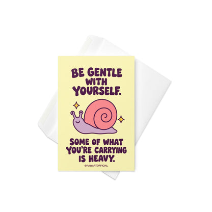 Heartfelt encouragement greeting card with a pastel yellow background and bold dark plum retro lettering reading “Be Gentle With Yourself. Some of What You're Carrying Is Heavy.” Features a smiling lavender snail with a large pink spiral shell and two golden sparkles. Gentle thinking-of-you and emotional support card by Hot Mess Paper Co.