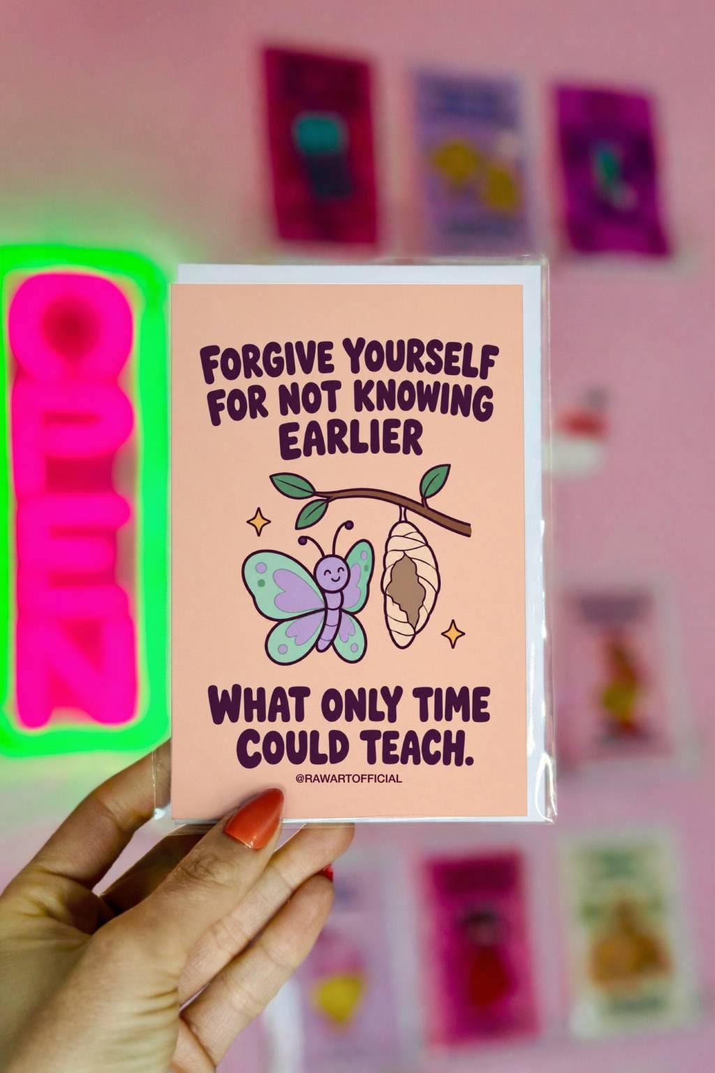 Self-forgiveness encouragement greeting card featuring a smiling pastel mint and lavender butterfly beside a hanging chrysalis on a leafy branch, with small golden sparkles. Soft peach background with bold dark plum retro lettering reading “Forgive Yourself for Not Knowing Earlier What Only Time Could Teach.” Inspirational personal growth and self-compassion card by Hot Mess Paper Co.