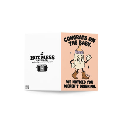 Funny pregnancy congratulations greeting card featuring a smiling cartoon baby bottle with a lavender collar, white gloves, and brown cowboy boots, waving on a peach background. Bold black retro lettering reads “Congrats on the Baby. We Noticed You Weren't Drinking.” Cheeky pregnancy announcement and expecting-parent congratulations card by Hot Mess Paper Co.