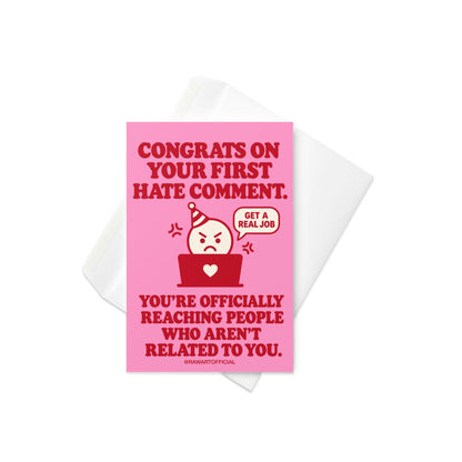 Funny content creator congratulations greeting card with a bright pink background and bold red retro lettering reading “Congrats on Your First Hate Comment. You're Officially Reaching People Who Aren't Related to You.” Features an angry cartoon character wearing a party hat behind a red laptop with a white heart, beside a speech bubble saying “Get a Real Job.” Humorous influencer milestone card by Hot Mess Paper Co.
