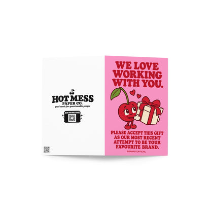 Pink influencer appreciation greeting card with bold red retro lettering reading “We Love Working With You. Please Accept This Gift as Our Most Recent Attempt to Be Your Favourite Brand.” Features a cute smiling red cartoon cherry holding a white gift box tied with a red ribbon, with two floating hearts. A playful brand collaboration thank you card for content creators and influencer PR packages.