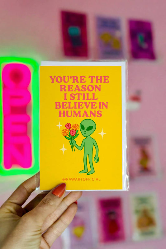 Greeting card featuring a green alien holding flowers with the text “You’re the reason I still believe in humans.”