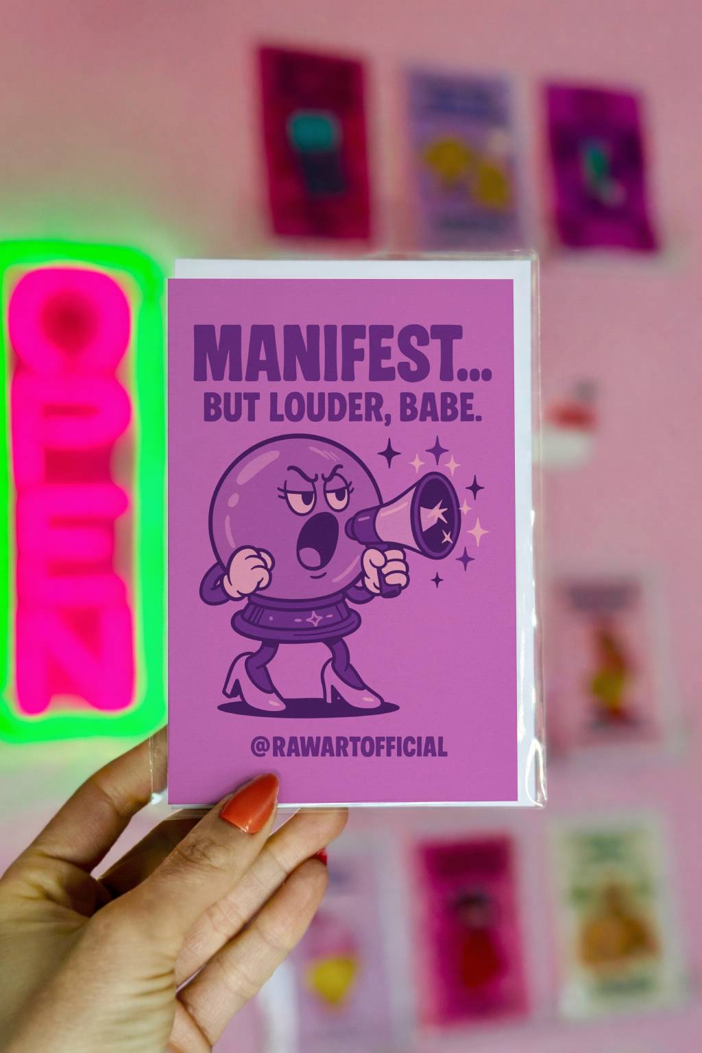 Greeting card featuring a cartoon crystal ball character shouting through a megaphone with the text “Manifest… But Louder, Babe.”