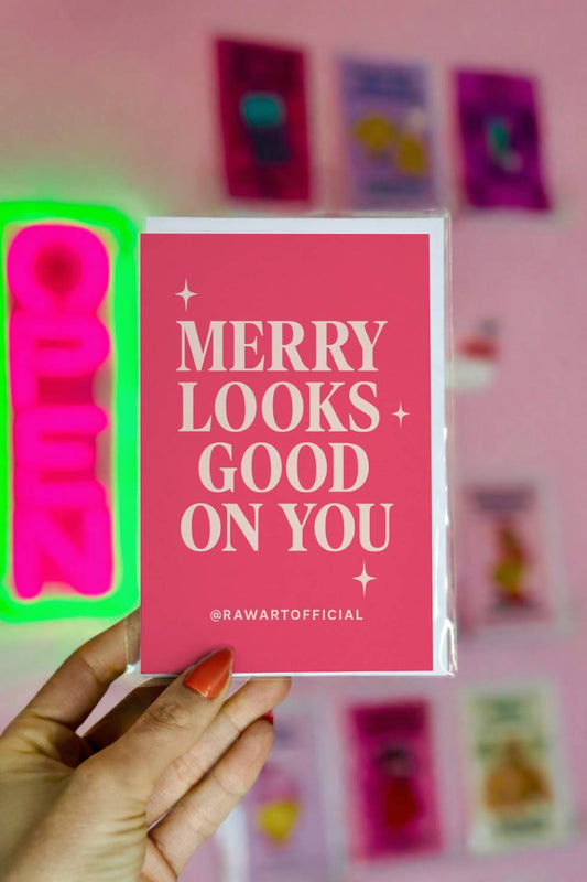 Pink minimalist Christmas card reading “Merry Looks Good On You” with retro typography and sparkle accents.