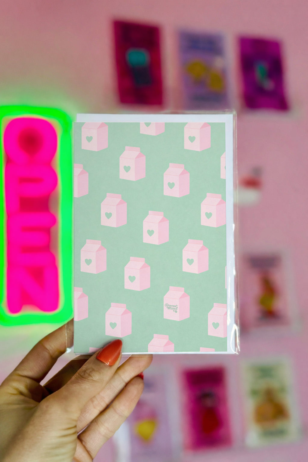 Notebook with pink milk carton pattern held by a hand against a pink wall with colorful posters.