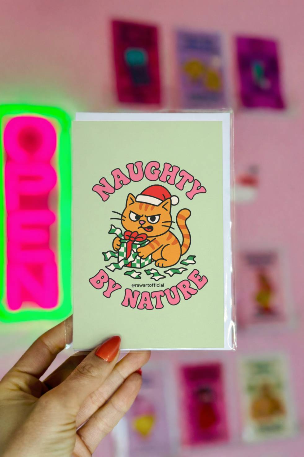 Funny Christmas card with mischievous orange cat wearing Santa hat tearing open a present with text “Naughty By Nature.”