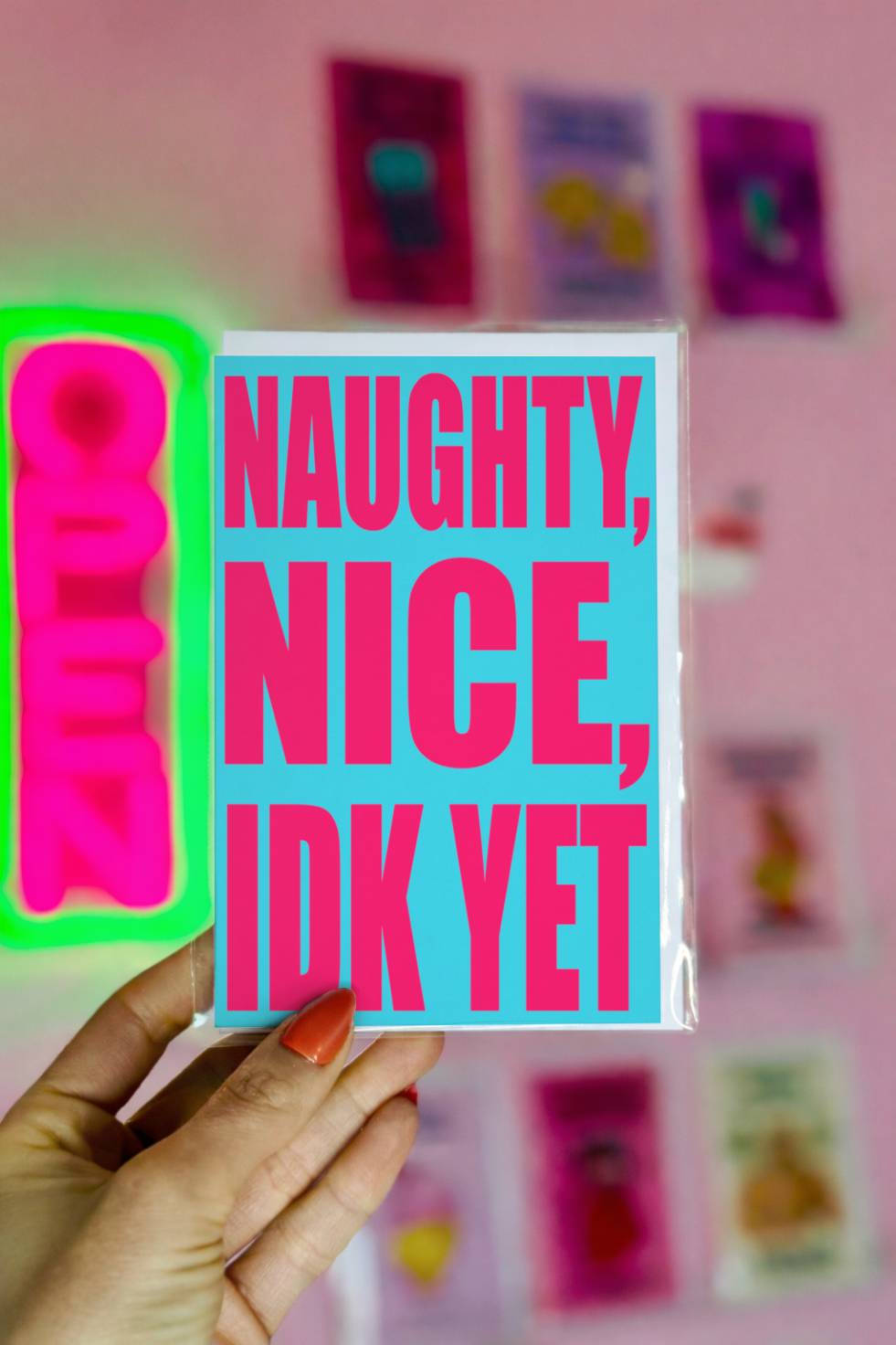 Funny Christmas greeting card with bold pink text reading “Naughty Nice I Don’t Know Yet” on a bright blue background.