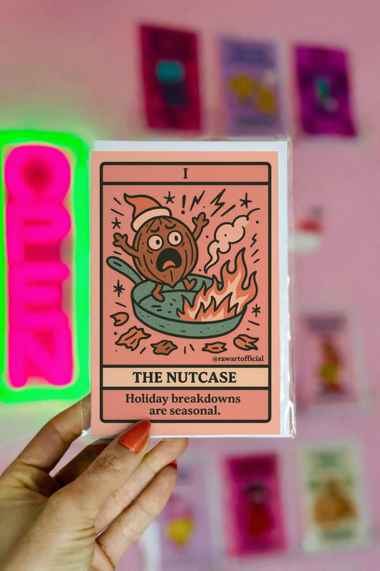 Retro tarot-style Christmas card featuring a panicked nut character in a frying pan with flames and text “The Nutcase – Holiday breakdowns are seasonal”