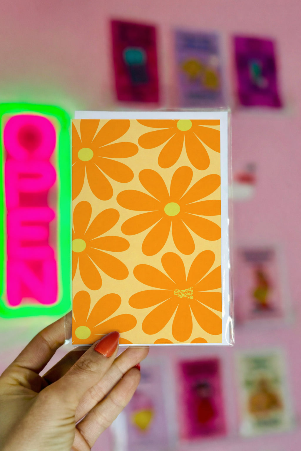 Hand holding a card with orange floral design against a pink background with colorful cards.